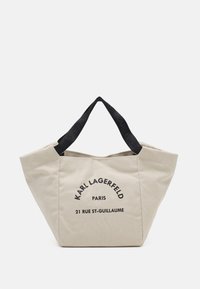 Borsa tote beige con testo nero "KARL LAGERFELD PARIS 21 RUE ST-GUILLAUME" sul davanti e manici neri con il nome del marchio impresso.