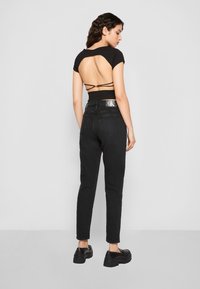 Fekete rövid cropped top nyitott hátsó résszel és pántos kivitelezéssel, magas derekú fekete farmerral és tömzsi fekete platform cipőkkel párosítva.