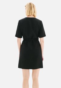 Robe noire à manches courtes avec une silhouette A-line simple et une taille ceinturée. Fabriquée en tissu texturé, avec un col rond.