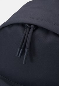 Mochila negra hecha de tela texturizada, con un cierre con cremallera y tiradores de cordón negros, y un pequeño detalle del logotipo.