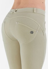 Jeans in denim elastic beige con una vestibilità slim, caratterizzati da cuciture decorative, due tasche posteriori e un piccolo badge con logo sulla tasca destra.