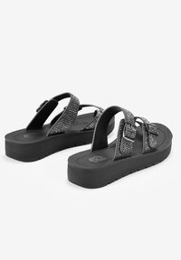 Chanclas negras con tiras texturizadas adornadas con strass, una plantilla acolchada y una suela de goma gruesa para mayor soporte.