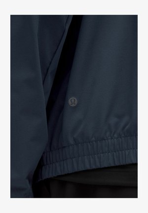 Marineblauwe windbreaker met elastische zoom en manchetten, gemaakt van glad, lichtgewicht materiaal; heeft een klein logo bij de zoom.