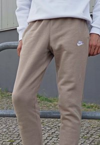 Béžové bavlnené tepláky so štíhlym strihom, s bielym logom Nike na ľavom stehne a elastickým pásom pre pohodlie.