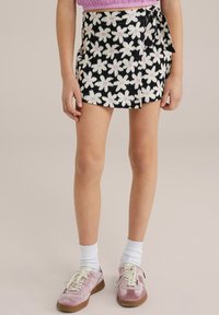 Black and white floral-patterned skirt with pink accents, featuring a wrap design and side tie. Worn with light pink sneakers and white socks.