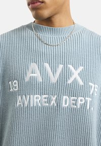 Lichtblauwe gebreide trui met ribbelstructuur, ronde hals en witte geborduurde tekst: "AVIREX DEPT." met de nummers "18" en "75."