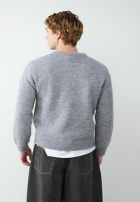 Grijze gebreide trui met lange mouwen, ronde hals en geribbelde zoom. De textuur lijkt zacht, met een overall gezellige uitstraling.