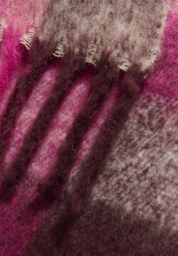 Uldtæppe med en gradient af pink, lilla og grå nuancer, med en blød, tekstureret overflade og frynse detaljer langs den ene kant.