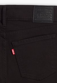 Crne traperice od denima s kožnom etiketom, crvenom Levi’s oznakom na džepu i suptilnim detaljima šivanja na stražnjem džepu.