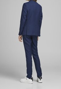 Granatowy garnitur o fakturowanym wykończeniu, z pojedynczym rozcięciem z tyłu, zestawiony z białymi trampkami z czarnymi akcentami.