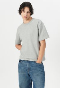 Grey cotton t-shirt with a crew neck, short sleeves, relaxed fit, paired with blue denim jeans. Subtle texture, simple design, no patterns.