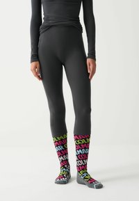 Fekete, hosszú ujjú felső, amely illeszkedő fekete leggings-szel van párosítva. Színes, többszínű zoknik, amelyek merész feliratokkal rendelkeznek sötét alapon. Egységes anyag, amely textúrázott.