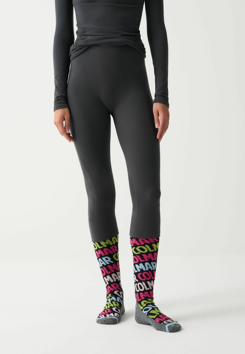 Fekete, hosszú ujjú felső, amely illeszkedő fekete leggings-szel van párosítva. Színes, többszínű zoknik, amelyek merész feliratokkal rendelkeznek sötét alapon. Egységes anyag, amely textúrázott.