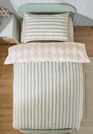 Einzelbett mit grün-weiß gestreiftem Kissen und Bettbezug, beiger Decke mit Diamantmuster, Holzboden und Nachttisch.