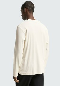 Langarm, ribbel T-shirt in gebroken wit, met een ronde hals en rechte onderkant. De stof lijkt zacht en comfortabel te zijn.