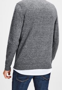 Grå tröja med en texturerad stickad design, rund halsringning och ribbad mudd. Lagd över en vit nederkant, ihop med blå jeans.