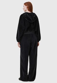 Svart velour träningsdräkt med en huva, elastisk midja och löst sittande byxor. Mjuk textur med en slät finish.