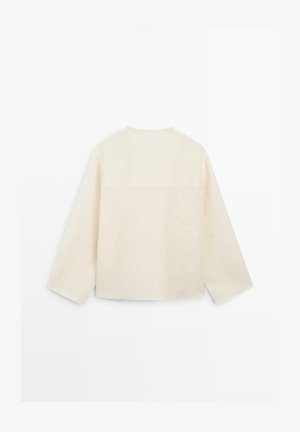 Camicia a maniche lunghe color crema con maniche larghe e orlo dritto, vista da dietro su sfondo bianco semplice.