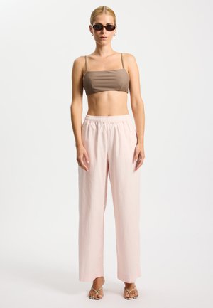 Top corto marrón con escote cuadrado y tirantes finos, combinado con pantalones anchos color rosa claro con textura de costillas verticales. Gafas de sol rectangulares transparentes.