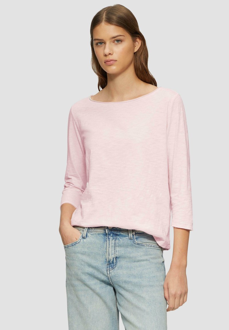 Haut rose clair à col bateau avec des manches trois quarts, fabriqué dans un tissu doux et texturé. Porté avec un jean en denim bleu clair taille haute.