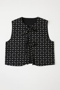 Melns bezroku veste ar teksturētu rakstu no mazām sudraba figūrām. Priekšējā daļā kaklasaites aizdare un A-līnijas siluets.