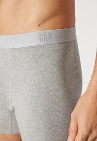 Grå herrebokser laget av et mykt stoff, med en lys grå elastisk midjebånd med "GAP" preget i matchende farge.