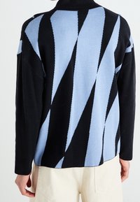 Black and light blue patterned knit sweater with a high collar and angular diamond shapes, featuring a relaxed fit and ribbed cuffs.