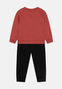 Red cotton sweatshirt with a round neckline and raglan sleeves, paired with black cotton sweatpants featuring a cuffed hem.