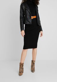 Giacca da motociclista nera in pelle con accessori in argento, abito nero aderente e stivaletti alla caviglia in stampa pitone color ocra con tacco a blocco.