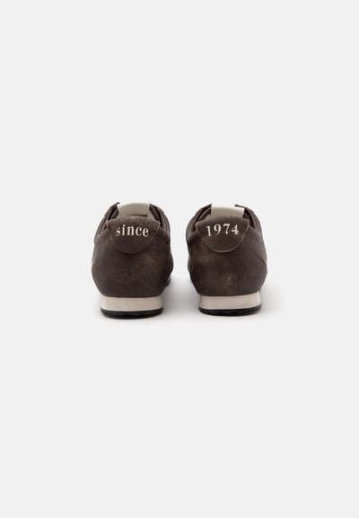 Paire de baskets marron foncé vues de dos avec un texte blanc sur les languettes de talon indiquant "since" à gauche et "1974" à droite.