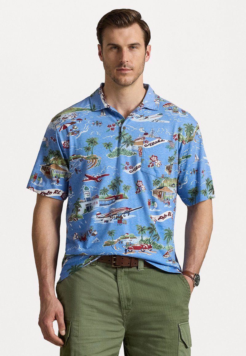 Polo de manga curta, azul, com um padrão tropical que apresenta aviões, palmeiras e cabanas. O material parece leve, texturizado, com um bolso.