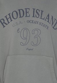 Szary hoodie z niebieskim nadrukiem: "RHODE ISLAND," "USA OCEAN STATE," oraz "'93 Original." Zawiera kieszeń z przodu, miękki materiał.