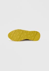 Gele rubberen schoenzool met getextureerde gripgroeven met hartpatronen en gestempelde logogegevens voor grip en stabiliteit.