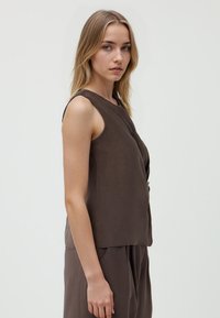 Top marrone senza maniche con una vestibilità rilassata, texture morbida e orlo arrotondato. Caratterizzato da un design drappeggiato delicato. Stile liscio e minimalista.