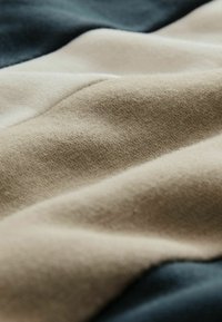 Tekstilstof i beige, elfenben og mørkeblå nuancer; har en blød tekstur med synlige strikkemønstre og subtile glatte folder.