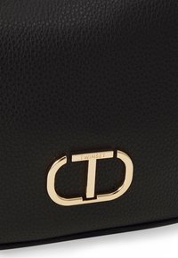 Zwarte leren tas met een gestructureerd oppervlak en gouden logo-accessoires met het woord "TWINSET" prominent afgebeeld.