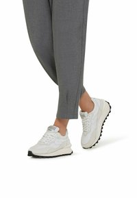Weiße Sneakers aus einer Mischung von Leder und Wildleder, mit einer strukturierten Sohle und einer gepolsterten Zunge. Kombiniert mit grauen, eng zulaufenden Hosen.