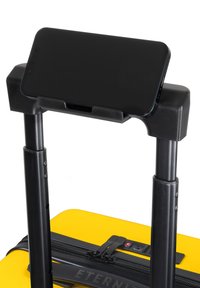 Un smartphone noir reposant sur un support en plastique noir fixé à une poignée télescopique de valise noire, avec une base de valise jaune vif visible.