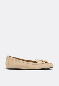 Mocassin femme en daim beige avec semelle plate, couture mocassin et pompons décoratifs à l'avant.