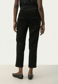 Black corduroy trousers with a straight leg design, two back pockets, and a cropped length, paired with black flats.