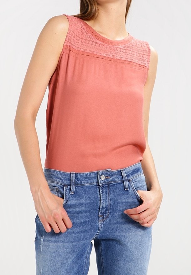 Ärmlös, korallfärgad topp med texturerad spetspanel vid axlarna, matchad med ljusblå denimjeans; mjukt tyg och avslappnad passform.