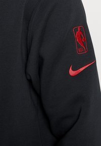 Sudadera negra de Nike con un logo de la NBA bordado en rojo en el hombro izquierdo y un acento del logo Nike en rojo en el pecho. Textura de tela suave.