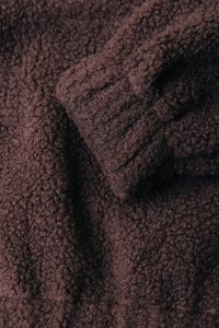 Tissu en polaire marron avec une surface texturée et duveteuse. Le matériau présente un poil épais et doux avec des nervures subtiles dans certaines zones.
