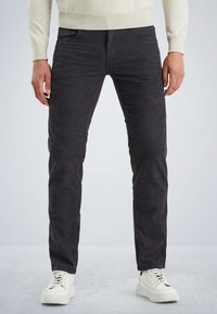 Jean slim gris foncé avec un motif texturé, comportant cinq poches et des détails de couture subtils, associés à des baskets blanches à lacets.