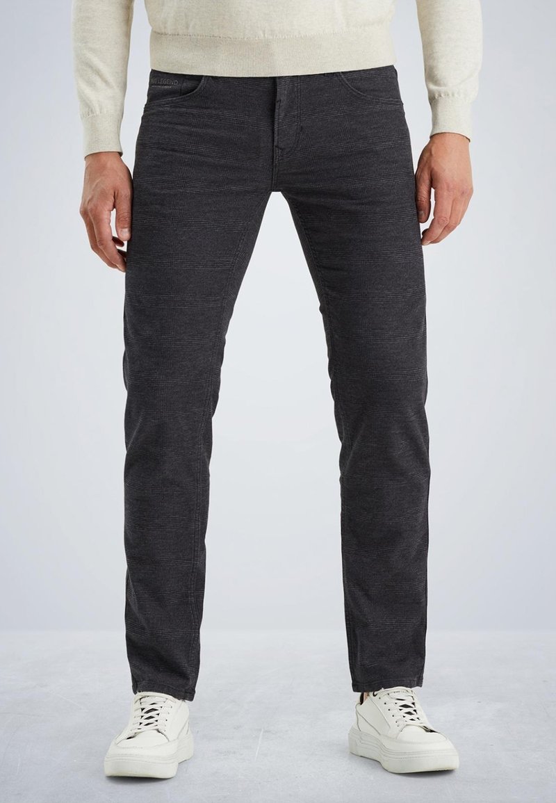 Jean slim gris foncé avec un motif texturé, comportant cinq poches et des détails de couture subtils, associés à des baskets blanches à lacets.