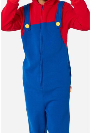 Enfant portant un sweat à capuche rouge et une salopette bleue avec des boutons jaunes, levant les deux bras sur un fond uni.
