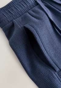 Joggers blu navy con tessuto strutturato, vita a coste e tasche laterali, realizzati in tessuto a maglia waffle per una maggiore traspirabilità e comfort.