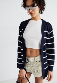 Cardigã às riscas navy com riscas brancas, textura de malha leve. Combinado com um top cropped branco e uma mini saia bege texturizada.