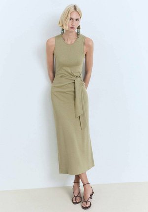 Robe sans manches vert olive avec un corsage ajusté et un détail noué à la taille, fabriquée en tissu doux, associée à des sandales à lanières.