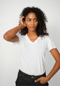White V-neck T-shirt made of cotton material, featuring short sleeves and a relaxed fit, paired with dark denim pants.